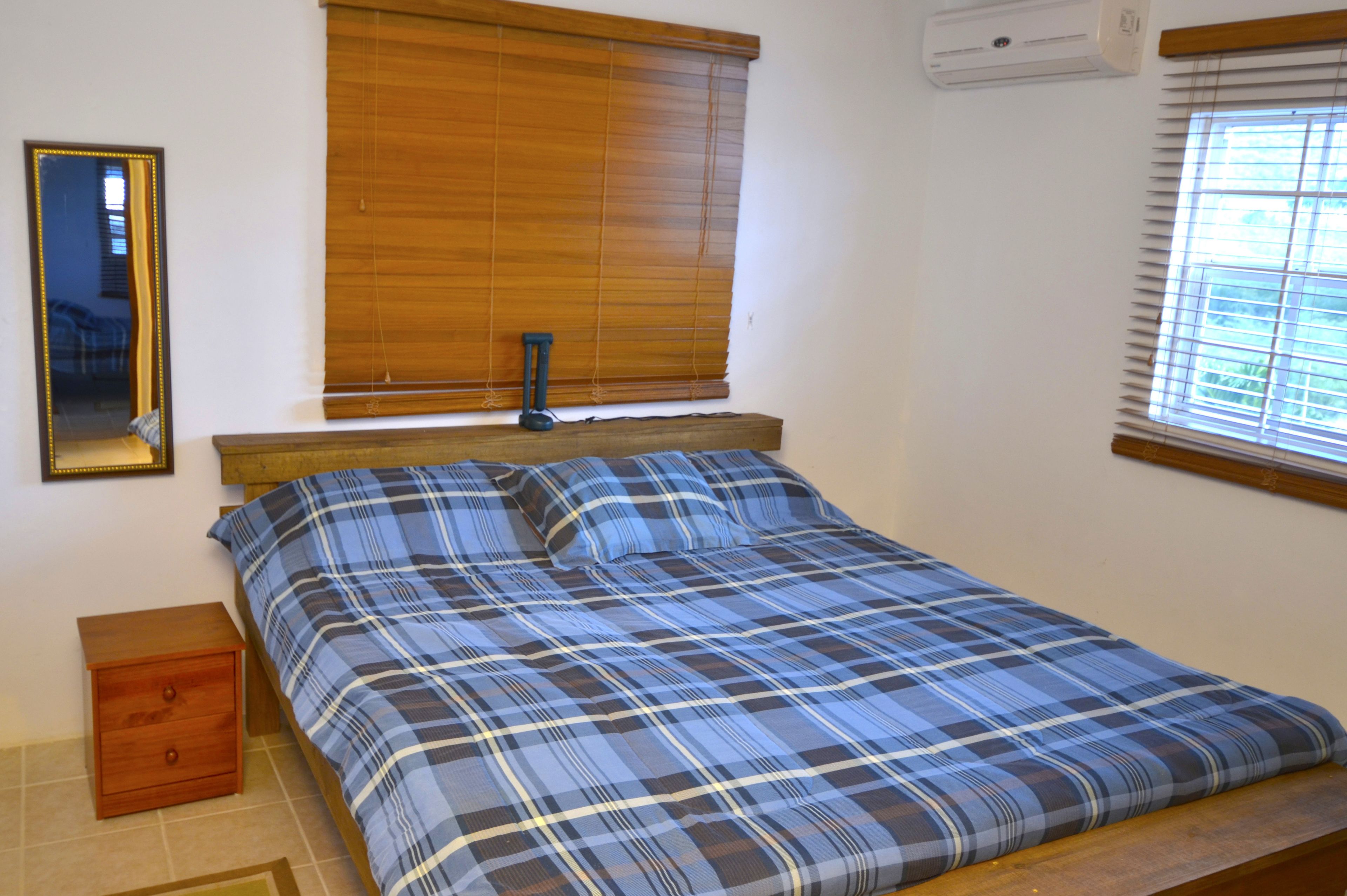Une chambre à coucher avec un lit, une table de chevet, un miroir et deux fenêtres équipées de stores.