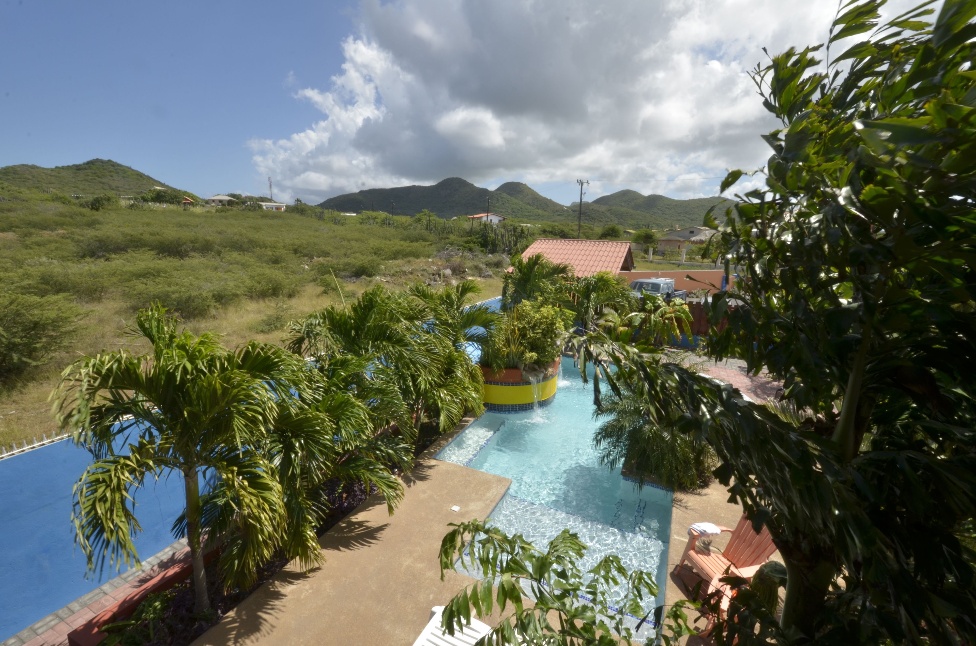 Resort com piscina rodeada por palmeiras e vista para colinas ao longe.