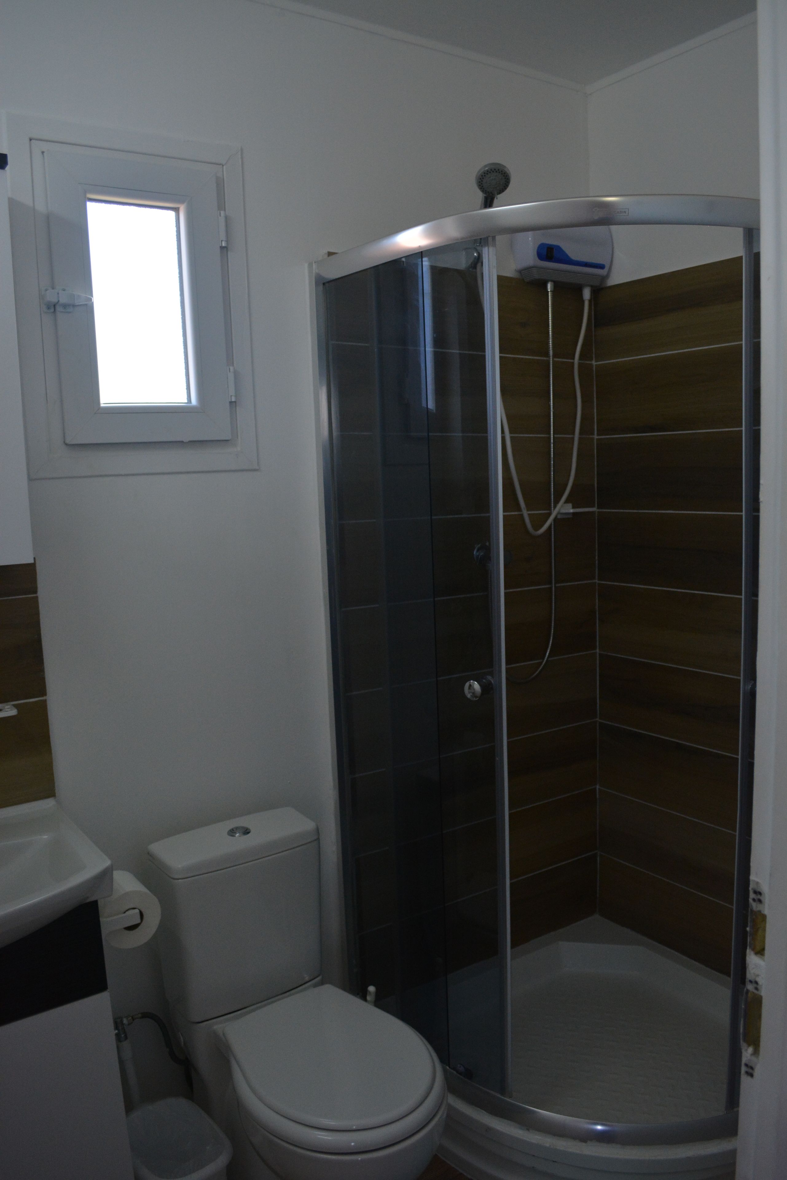 Un baño con ducha acristalada, inodoro y ventana sobre la puerta.