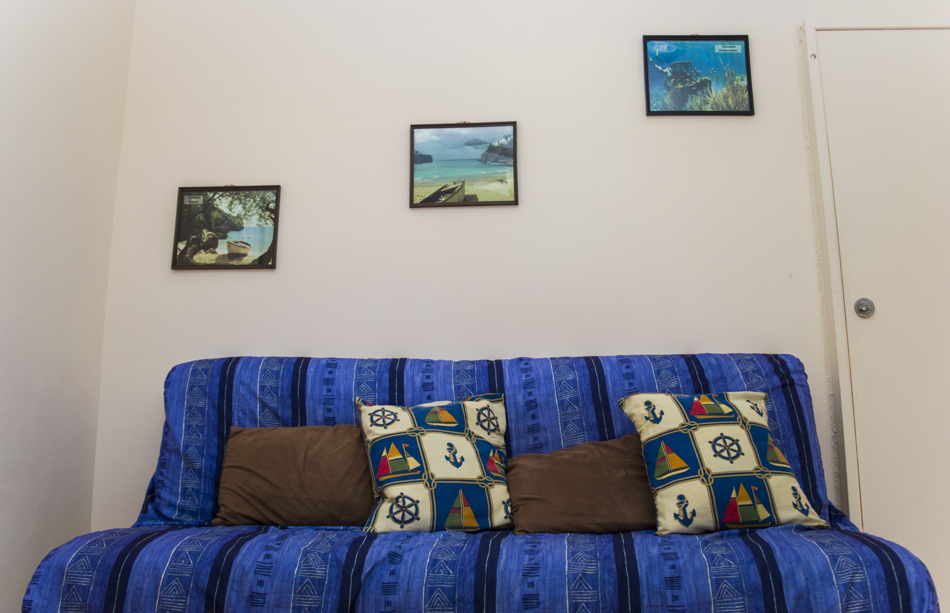 A room with a blue-striped sofa, two brown cushions, and three framed pictures on the wall.
