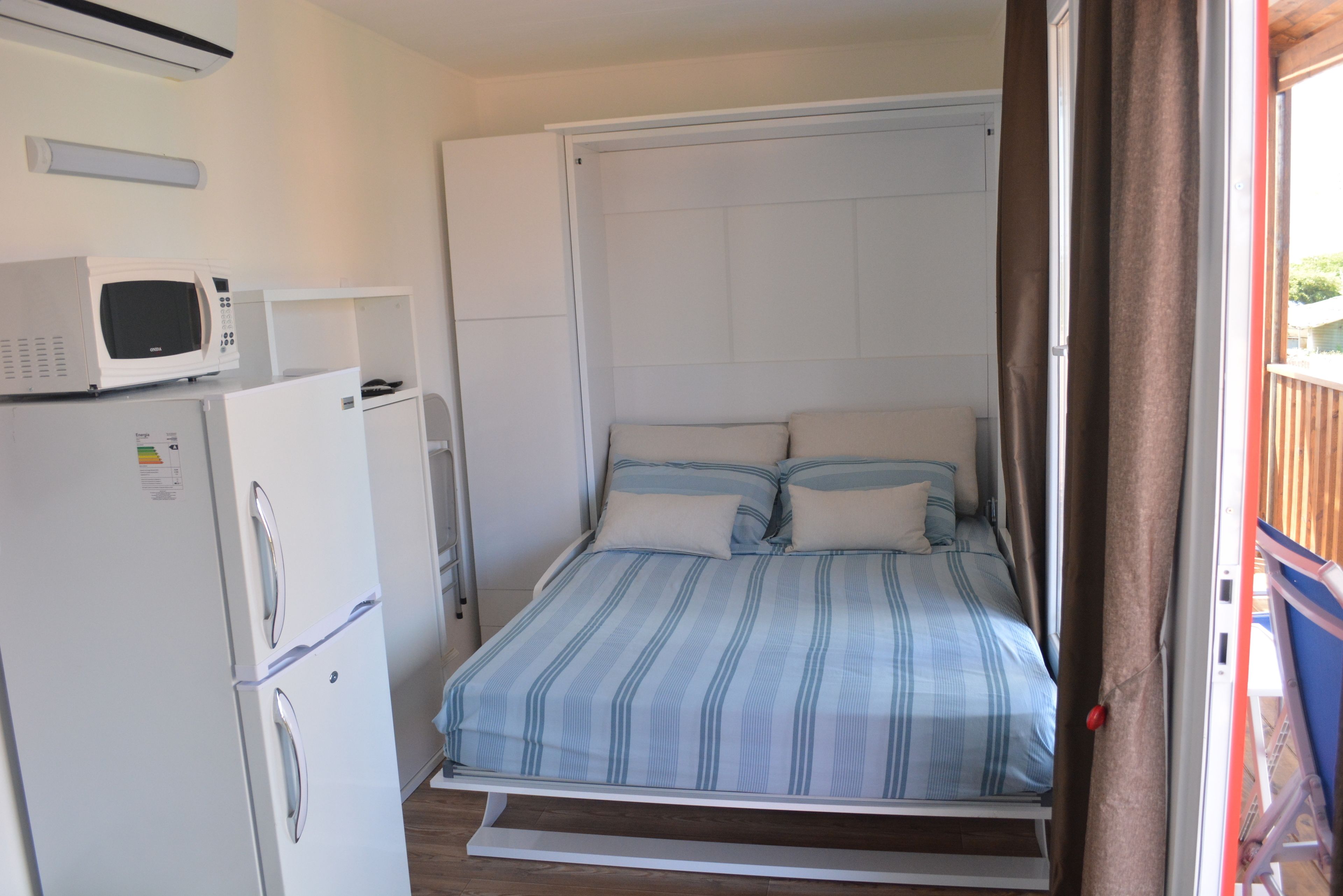 Une petite chambre comprenant un lit, un réfrigérateur blanc et un four à micro-ondes posé sur le dessus.