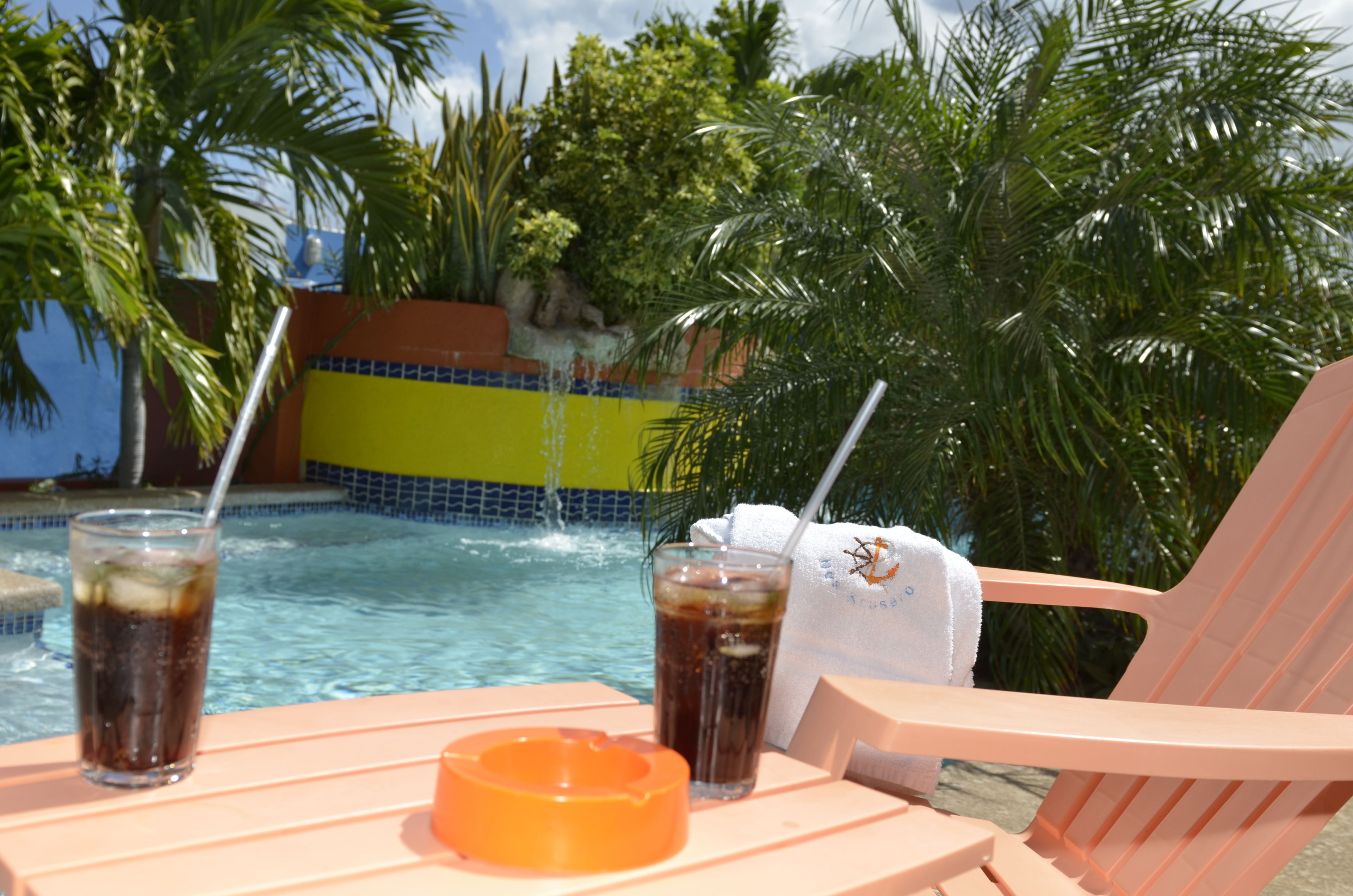 A poolside setting with a chair, a glass of soda, and a glass of iced tea.
