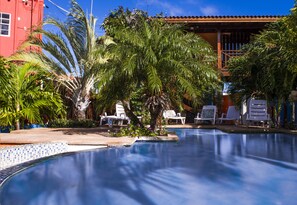 A swimming pool with lounge chairs and palm trees. - Nos Krusero Apartments (Sabana Westpunt)