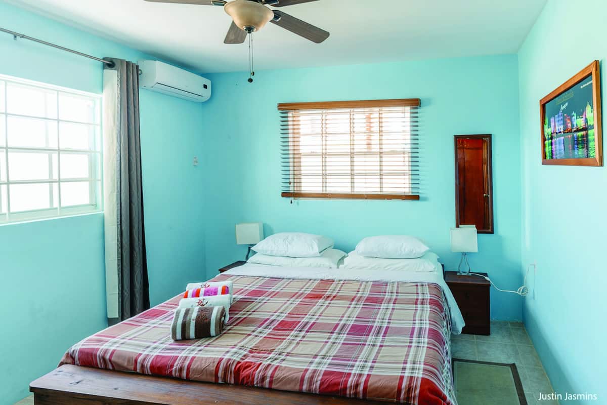 Una camera da letto con un letto, una ventola a soffitto, una finestra con persiane, un comodino e un condizionatore d'aria a parete.