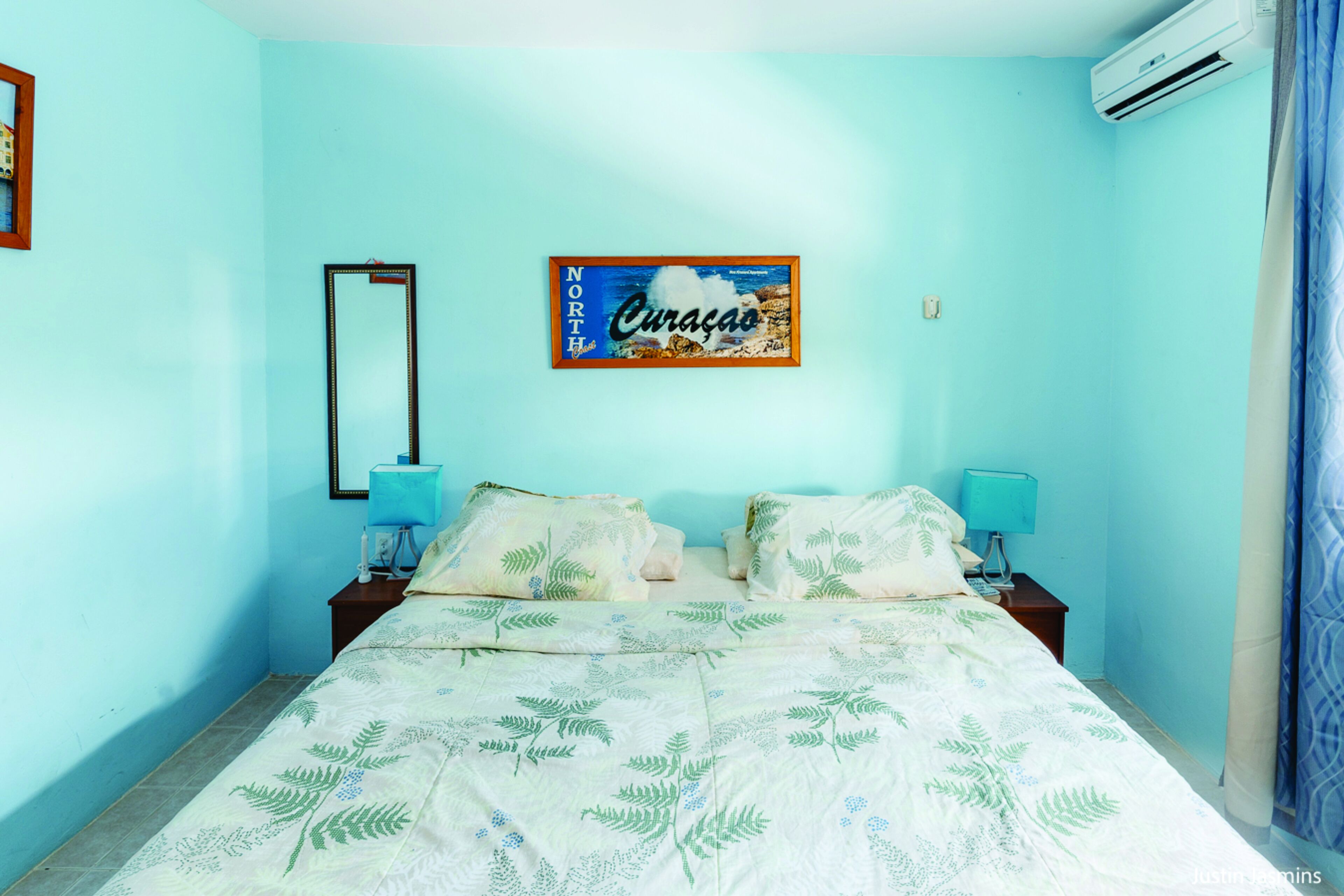 A bedroom with a bed, two bedside tables, a mirror, and a framed picture on the wall.