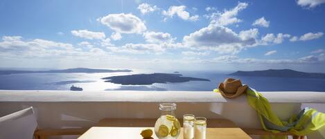 A wooden table with a glass pitcher, two glasses, and a lemon on a balcony overlooking a sea view.