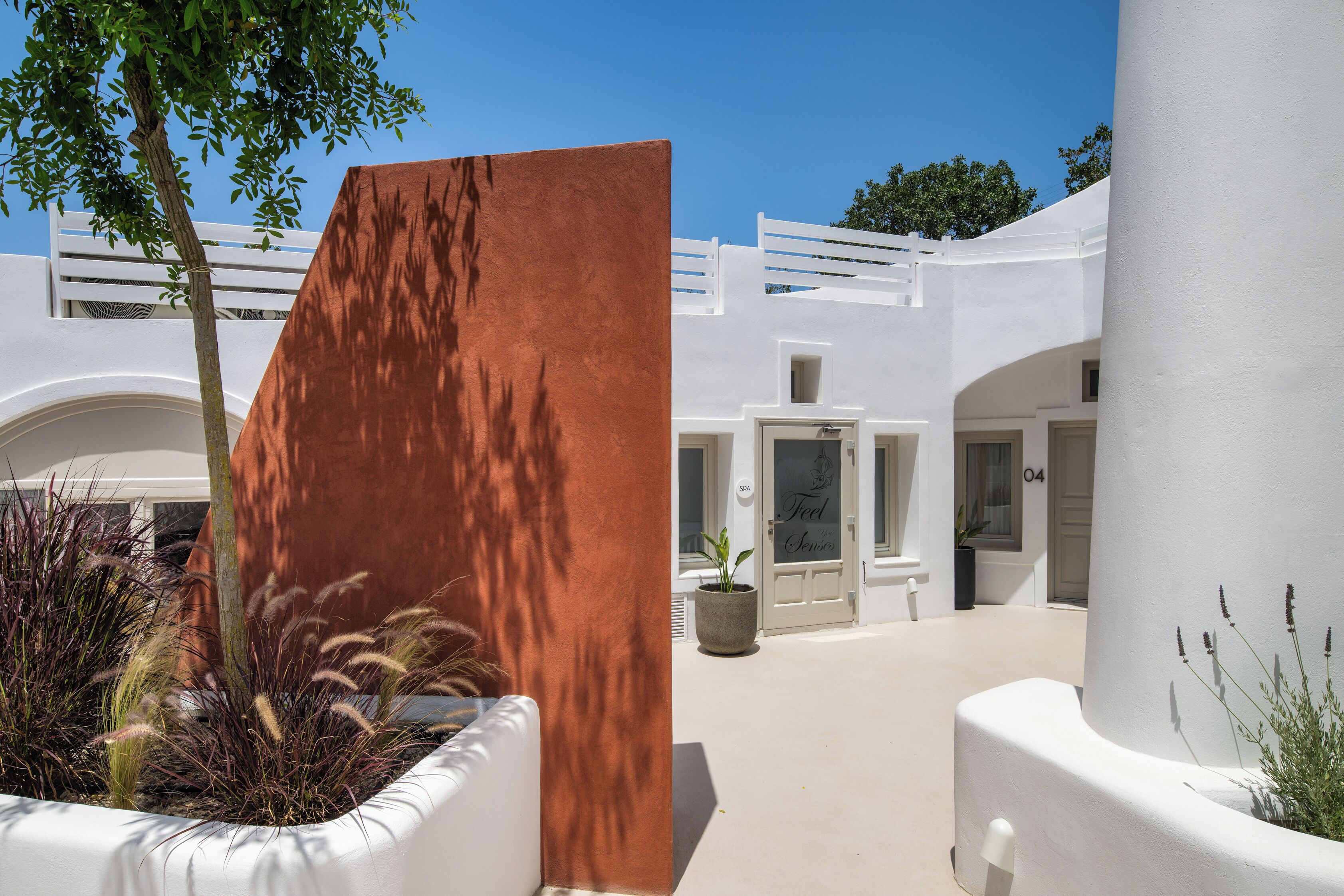 A white building with a curved entrance, potted plants, and a tree.