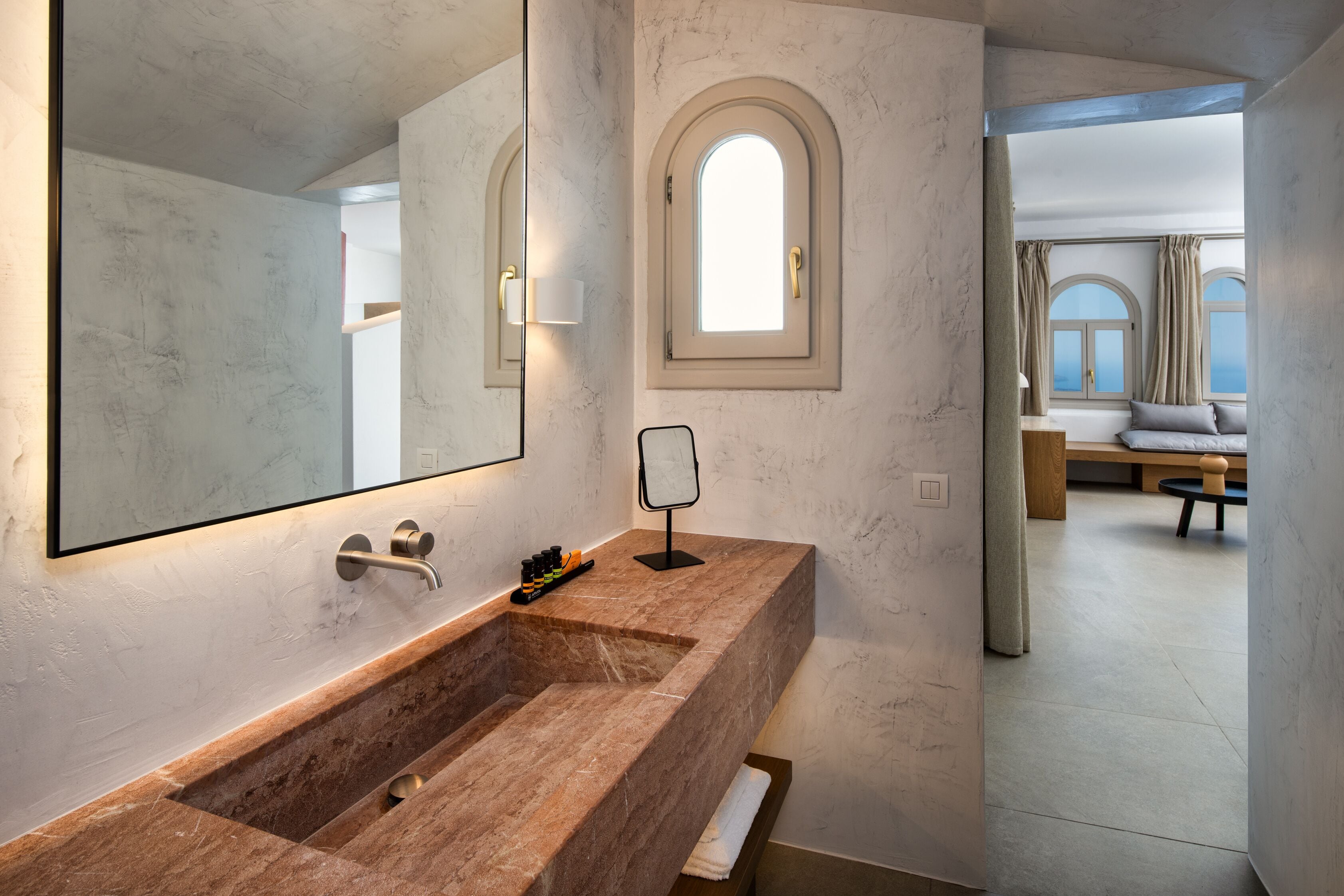Une salle de bain avec un lavabo en marbre, un grand miroir et une fenêtre avec des rideaux.