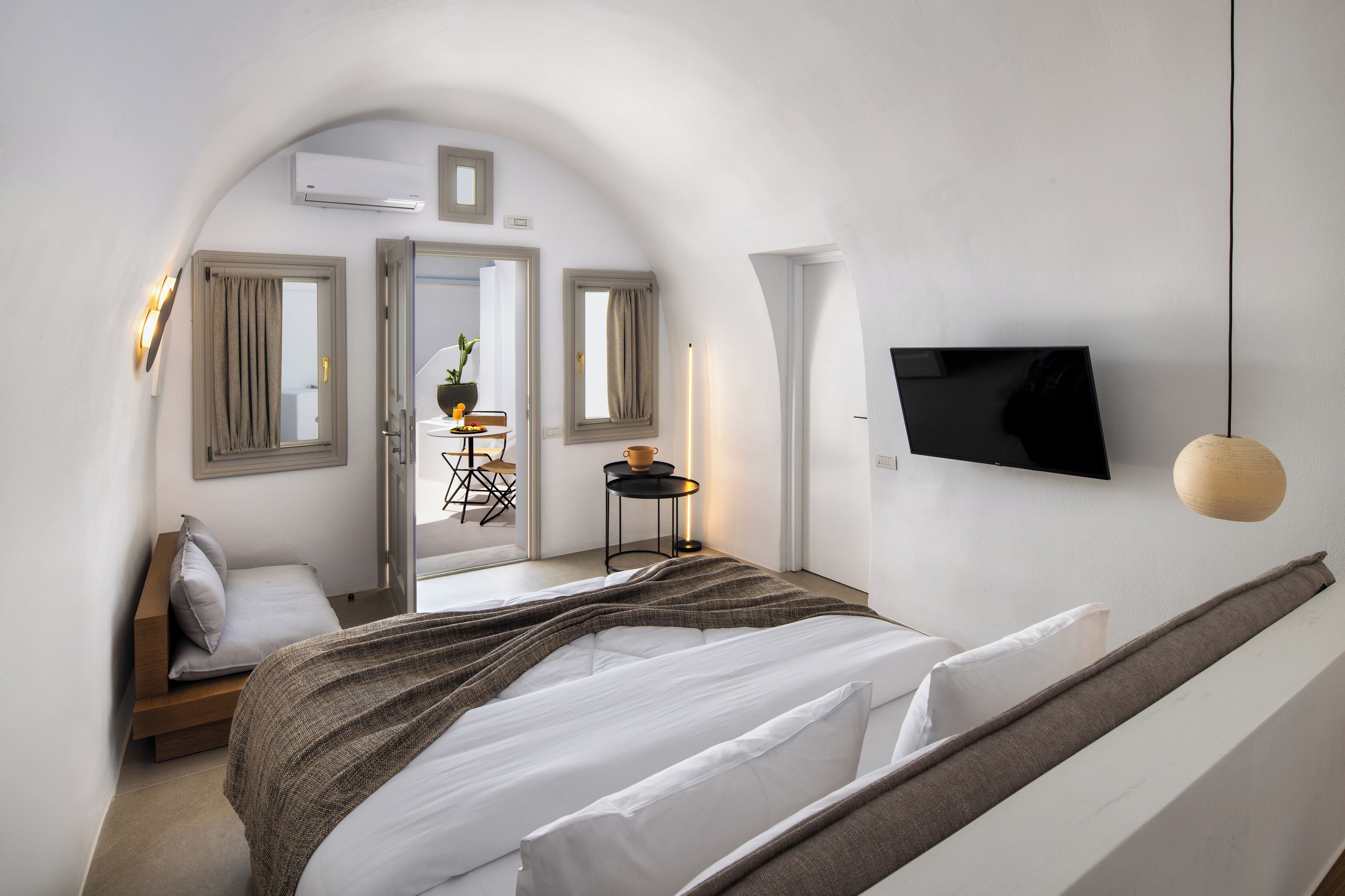 Un dormitorio moderno con cama, televisor y una mesita con una planta.