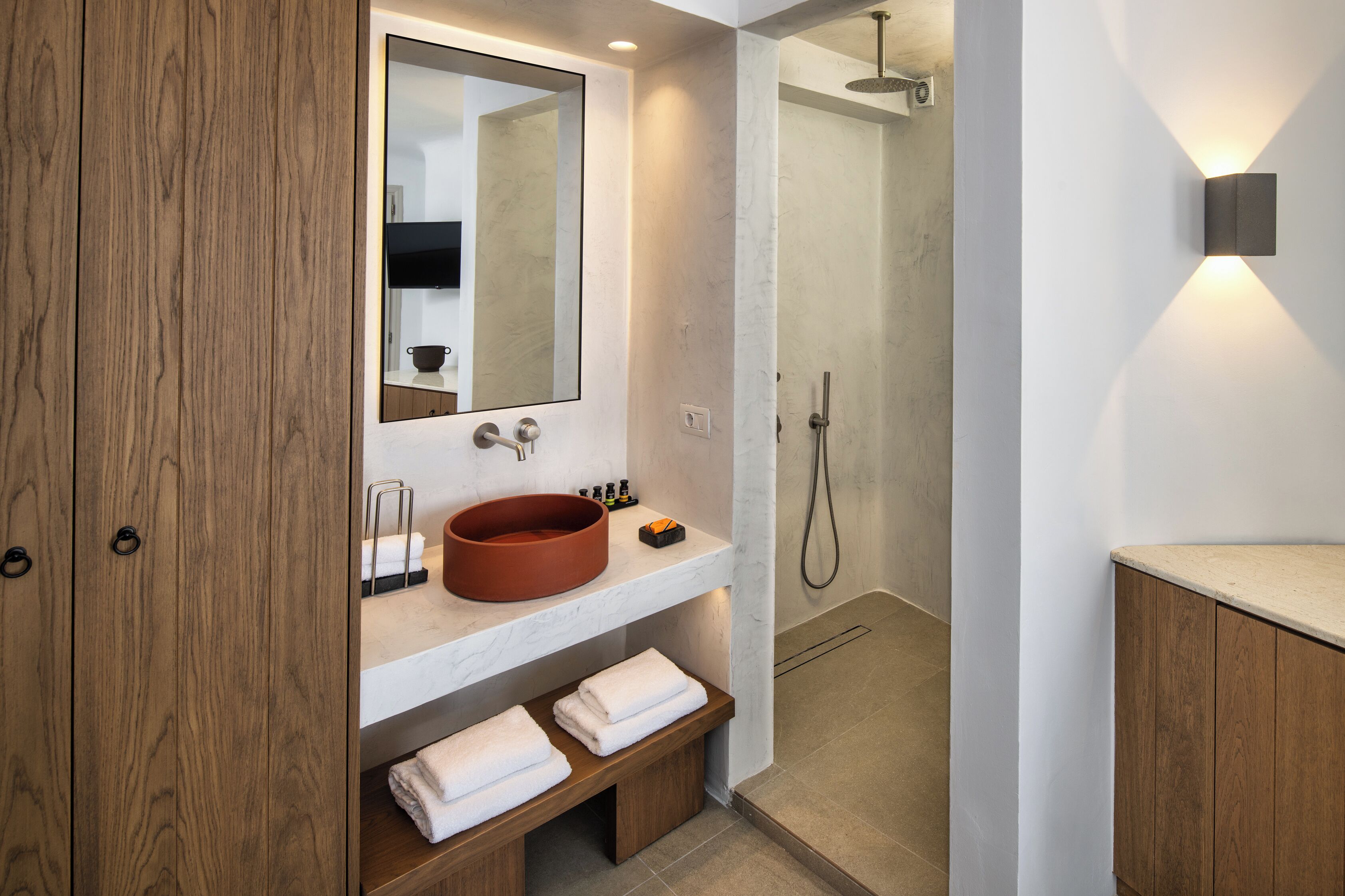 A modern bathroom with a wooden vanity, a round sink, a mirror, and a shower area.