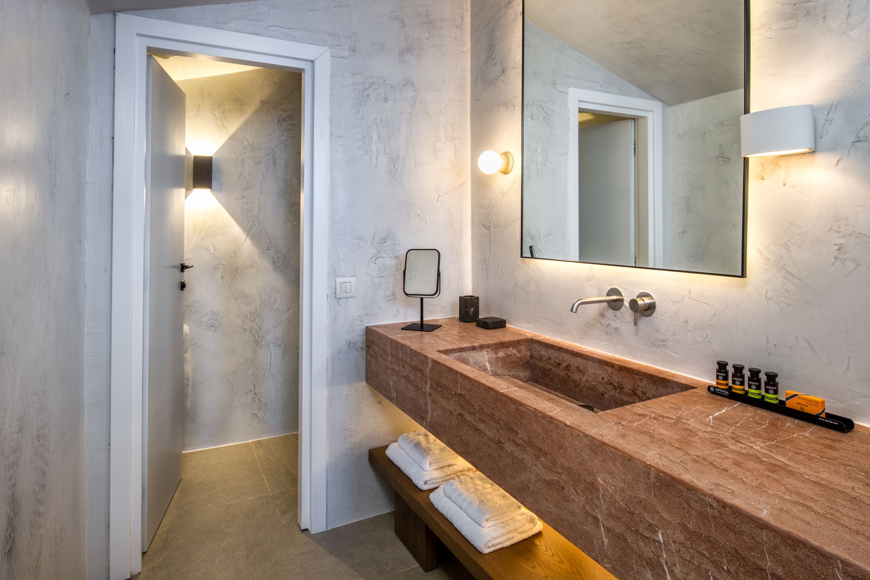 A bathroom with a marble sink, a mirror, and a bench with towels.