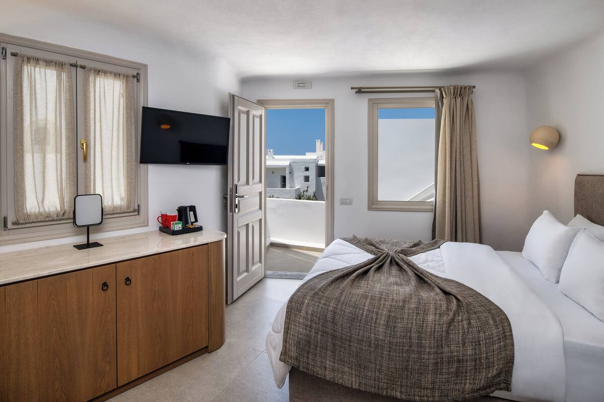 A hotel room with a bed, a TV, a coffee maker, and a view of the outside.