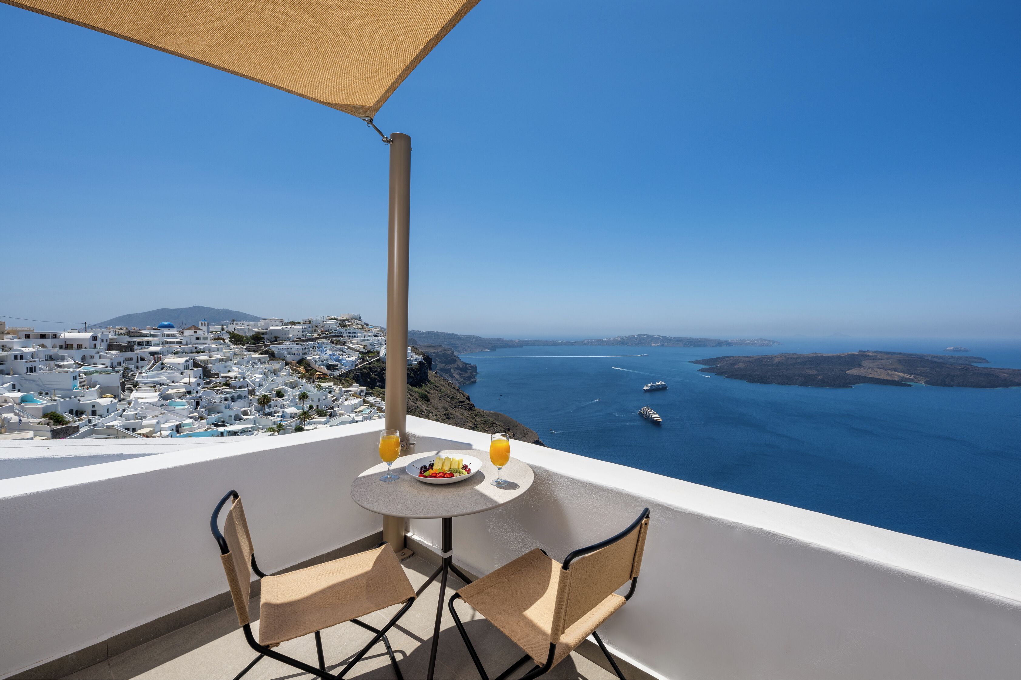 A balcony with a table and chairs overlooking a coastal town and the sea.