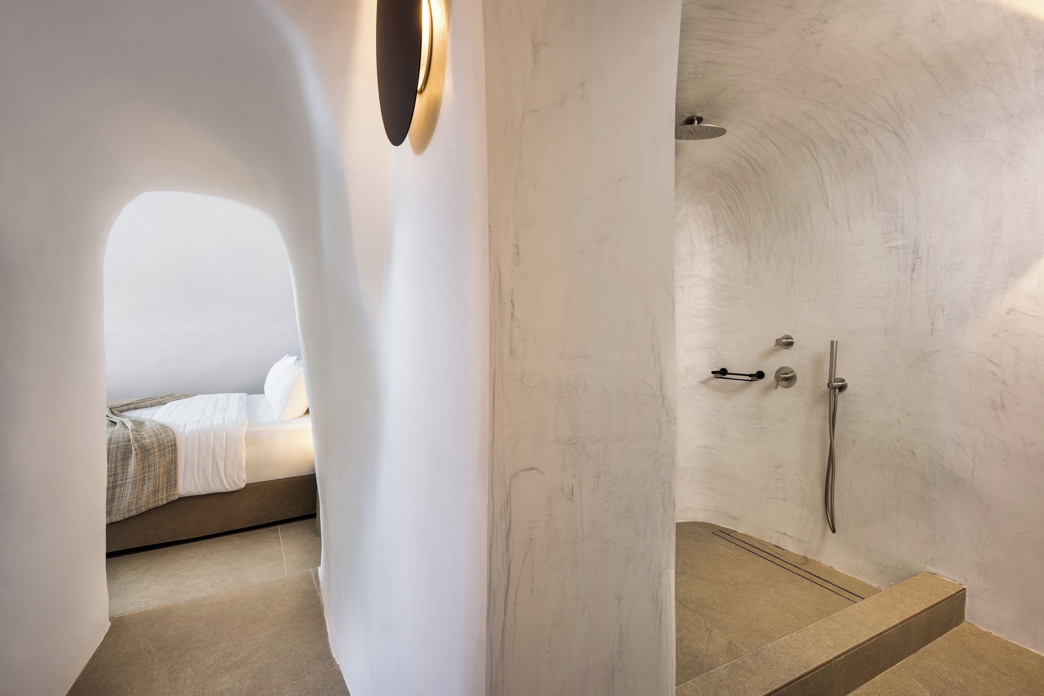 Een moderne badkamer met een douche, een zichtbaar bed in de aangrenzende kamer en een uniek architectonisch ontwerp.