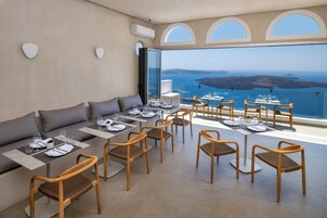 Un comedor con mesas y sillas, un sofá y un amplio ventanal con vista al mar.