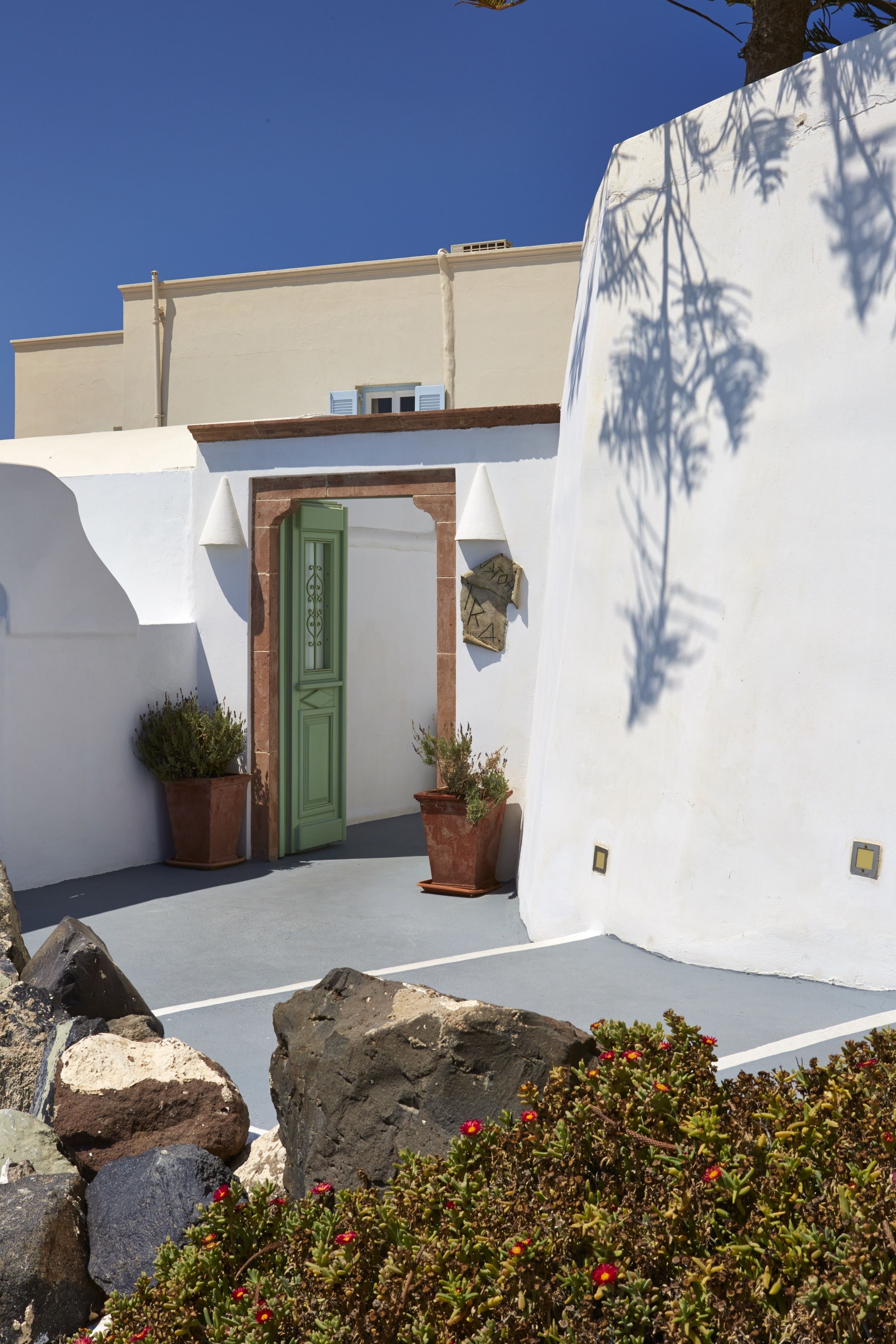 A courtyard with a green door, potted plants, and a white wall.