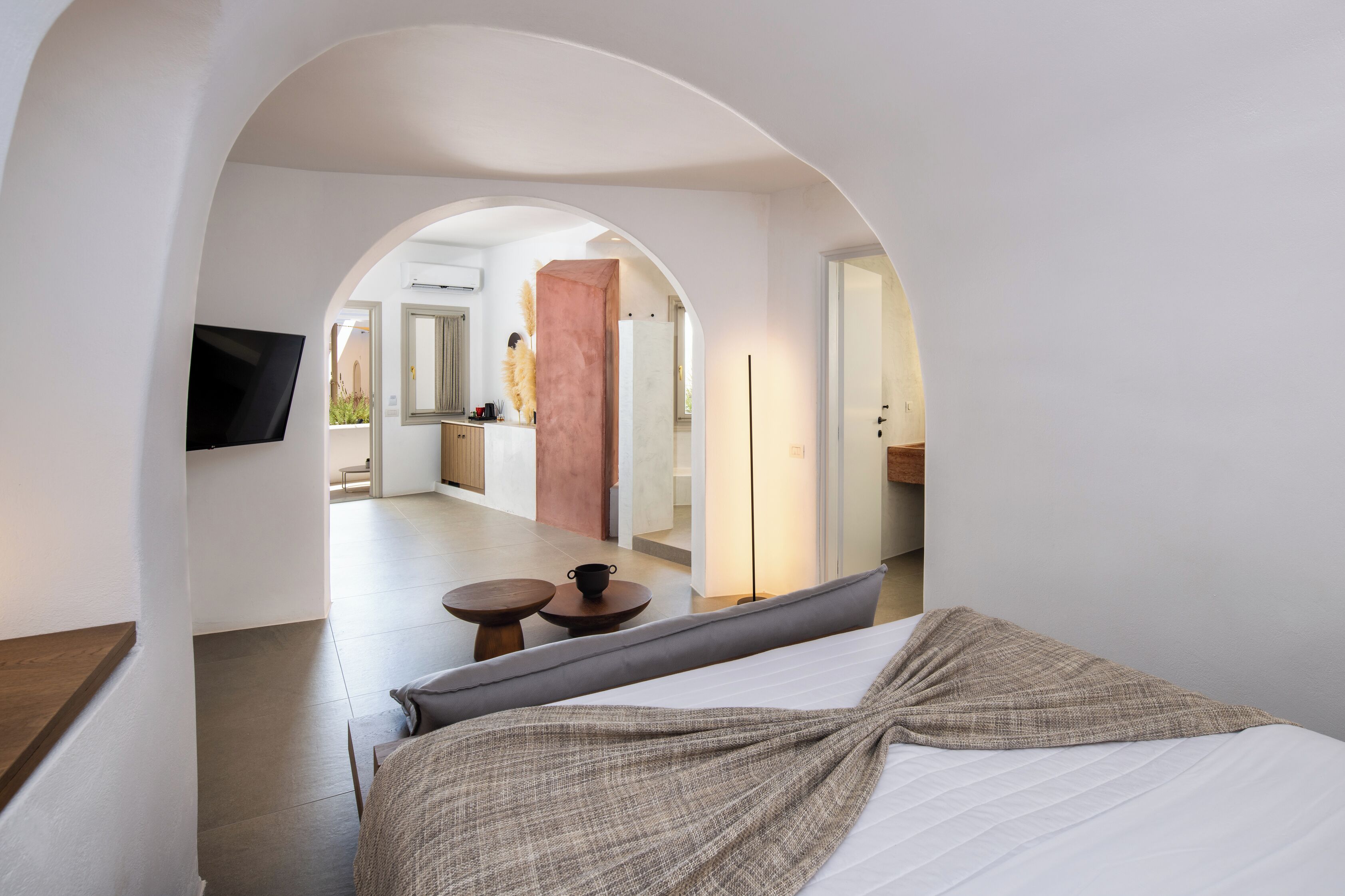 A hotel room with a bed, a TV, a small table, and an arched doorway leading to a bathroom.