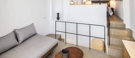 Un espacio habitable moderno y minimalista con un sofá, una mesa de centro y una escalera que lleva a un dormitorio.