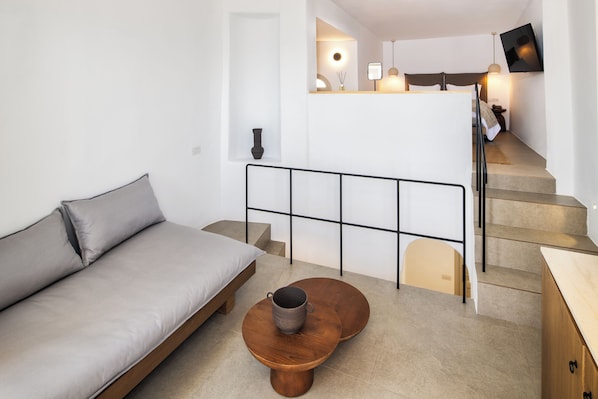 Un espacio habitable moderno y minimalista con un sofá, una mesa de centro y una escalera que lleva a un dormitorio.