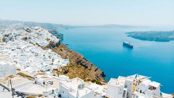 A coastal town with white buildings, a clear blue sea, and a cruise ship in the distance.