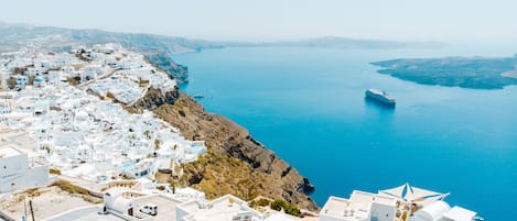 A coastal town with white buildings, a clear blue sea, and a cruise ship in the distance.