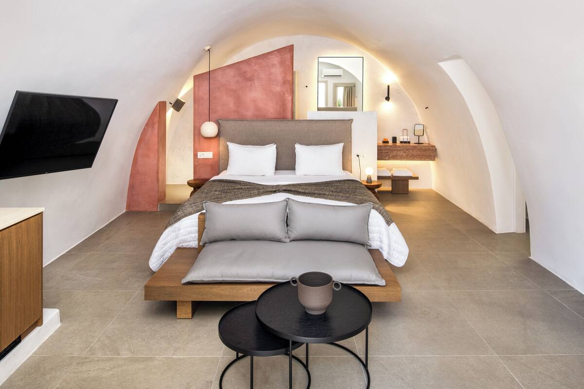 A modern bedroom with a large bed, a TV mounted on the wall, a bedside table, and a small table with a cup.