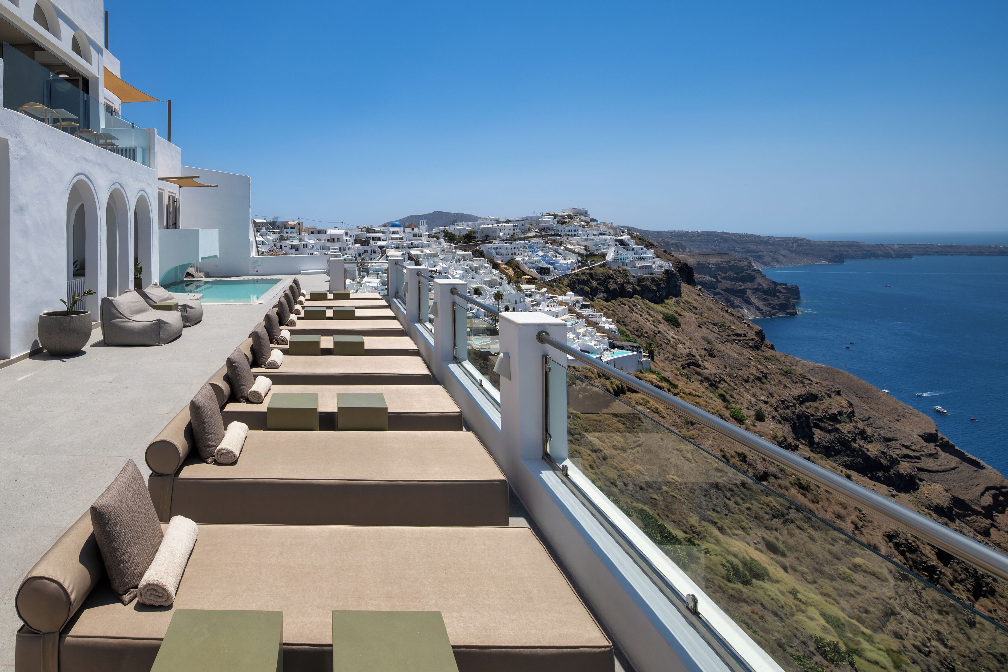 Une terrasse sur le toit avec une piscine, des espaces de détente en plein air et une vue sur une ville côtière.