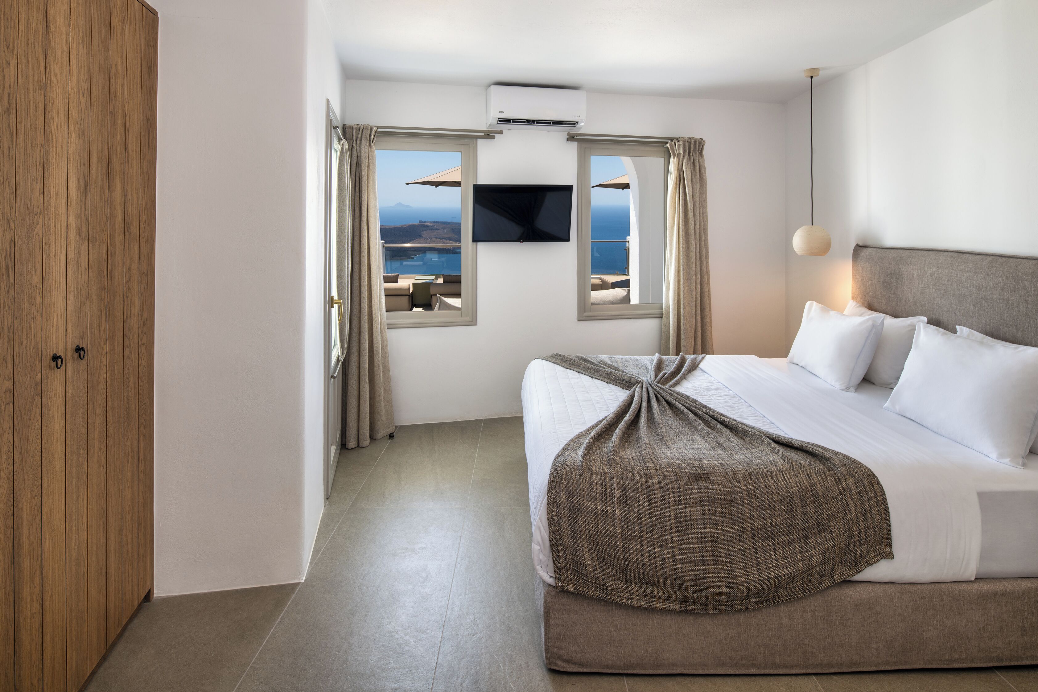 A hotel room with a bed, a TV, and a view of the sea.