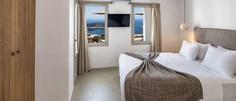 A hotel room with a bed, a TV, and a view of the sea.