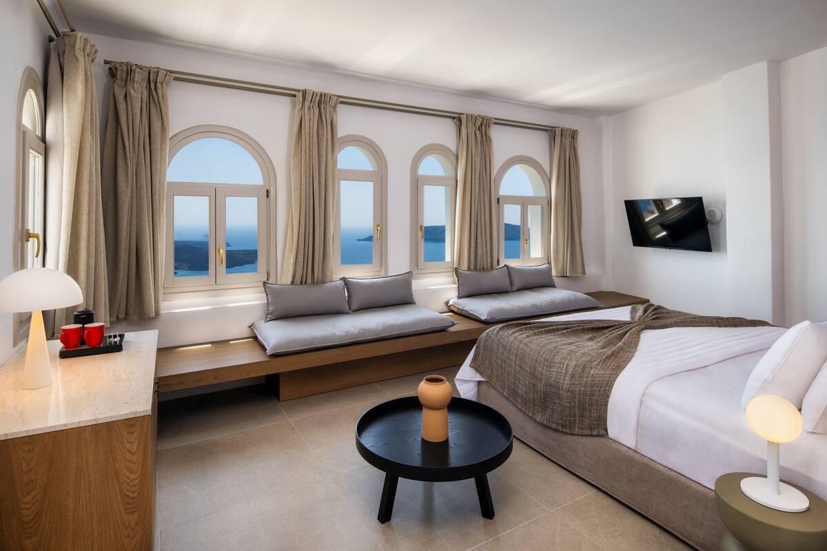 A modern hotel room with a large bed, a sofa, a small table, and a TV.