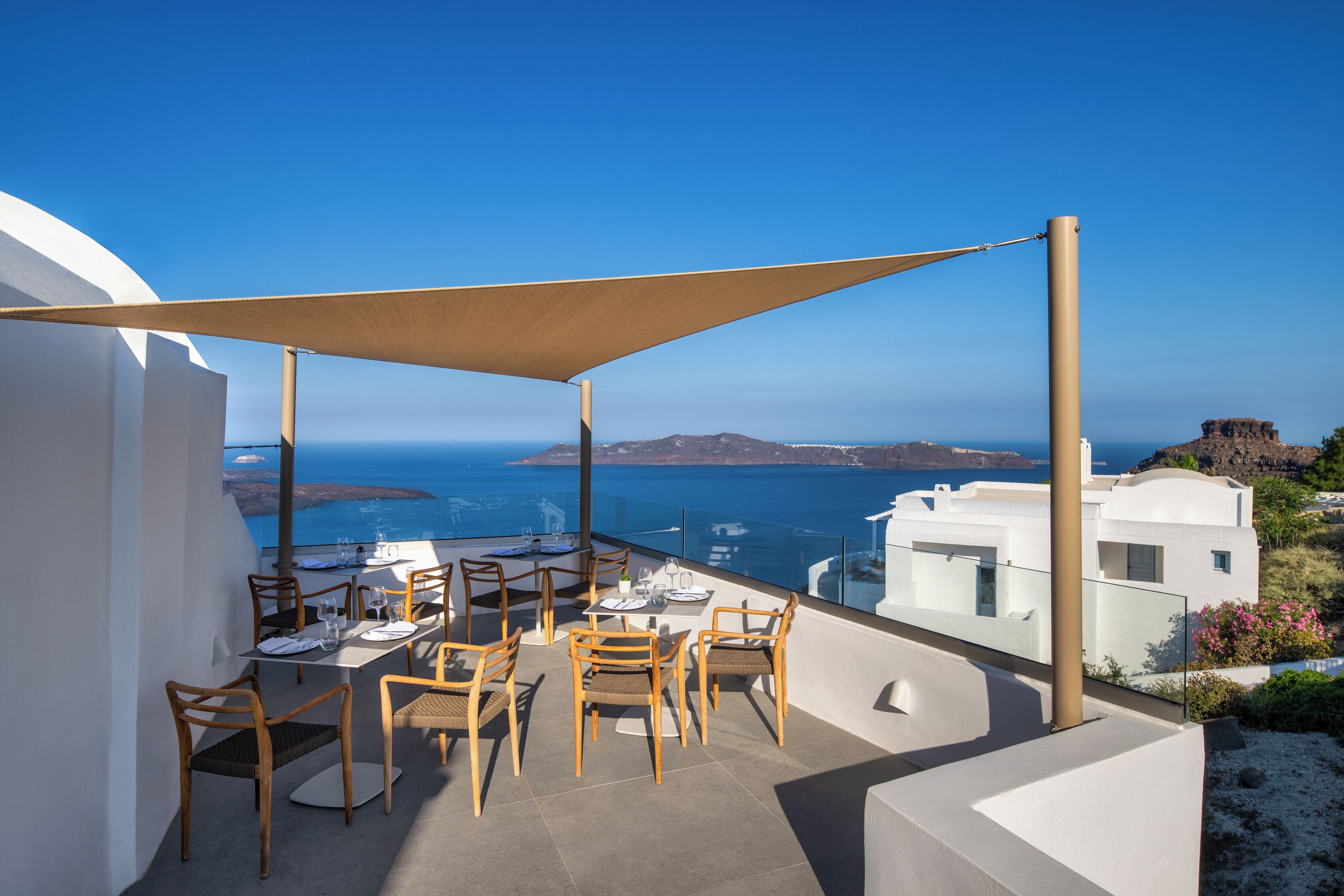 Une terrasse agrémentée de tables et de chaises, offrant une vue sur un paysage côtier avec des bâtiments et la mer.