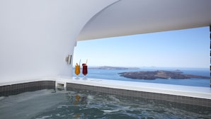 A bathtub with a view of the sea, two glasses of red wine, and a small table.