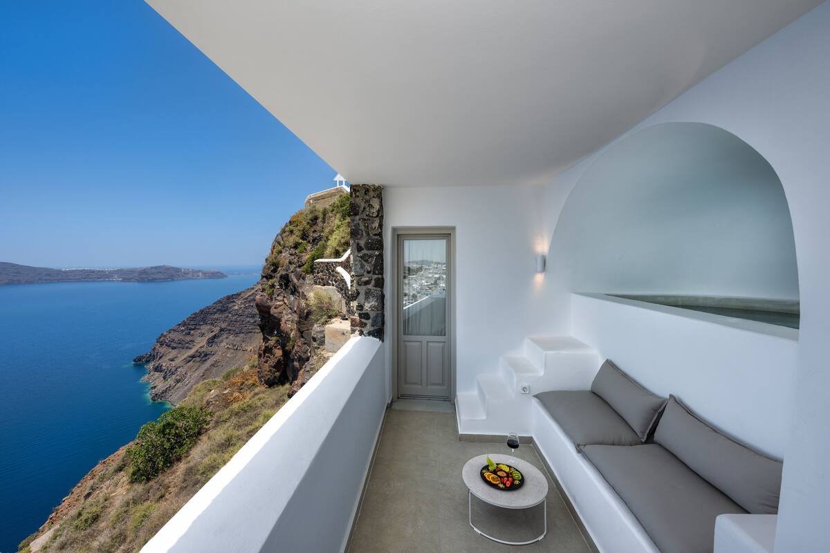 A balcony with a stone wall, a sofa, a small table with fruit, and a view of the sea.