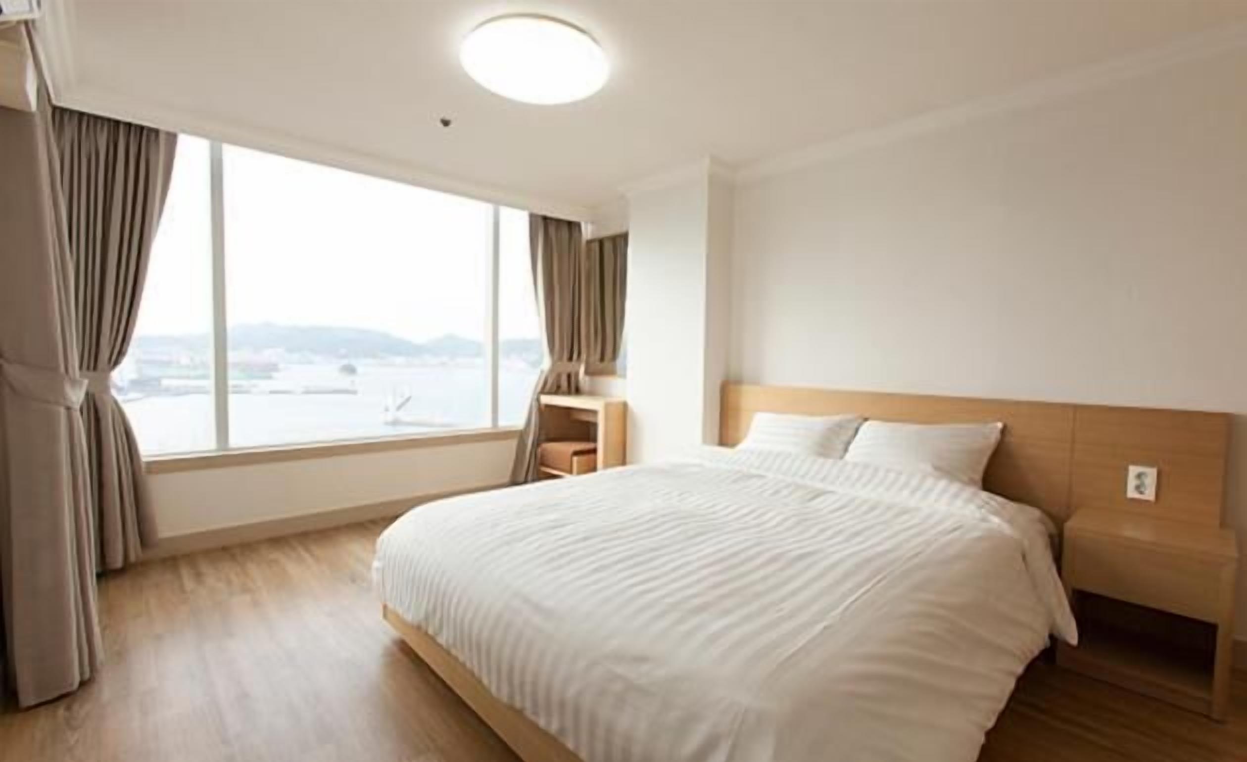 A hotel room with a large bed, a nightstand, a chair, and a view of the water.
