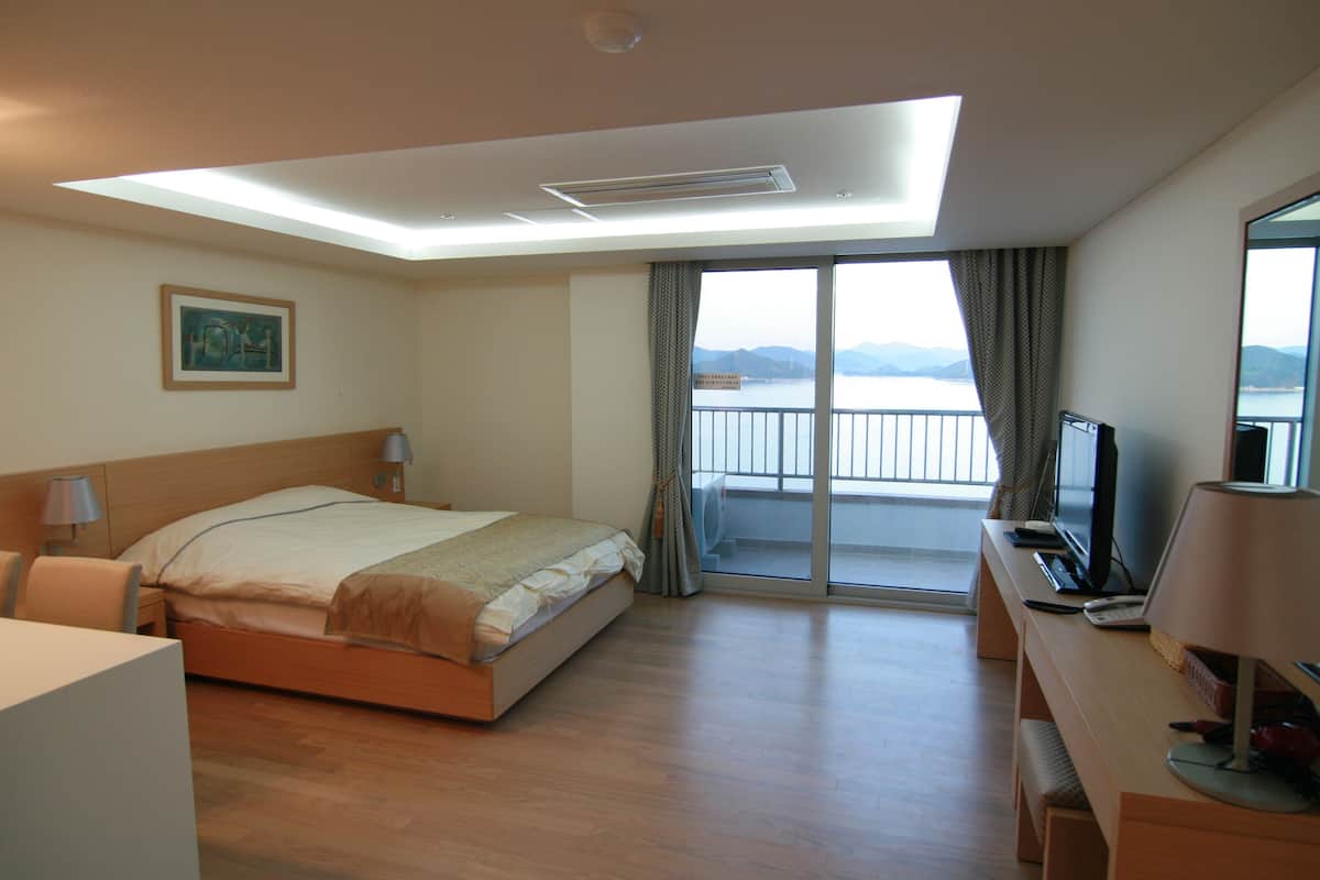 Une chambre d’hôtel équipée d’un lit, d’un bureau, d  ’un ordinateur et offrant une vue sur la mer par la fenêtre.
