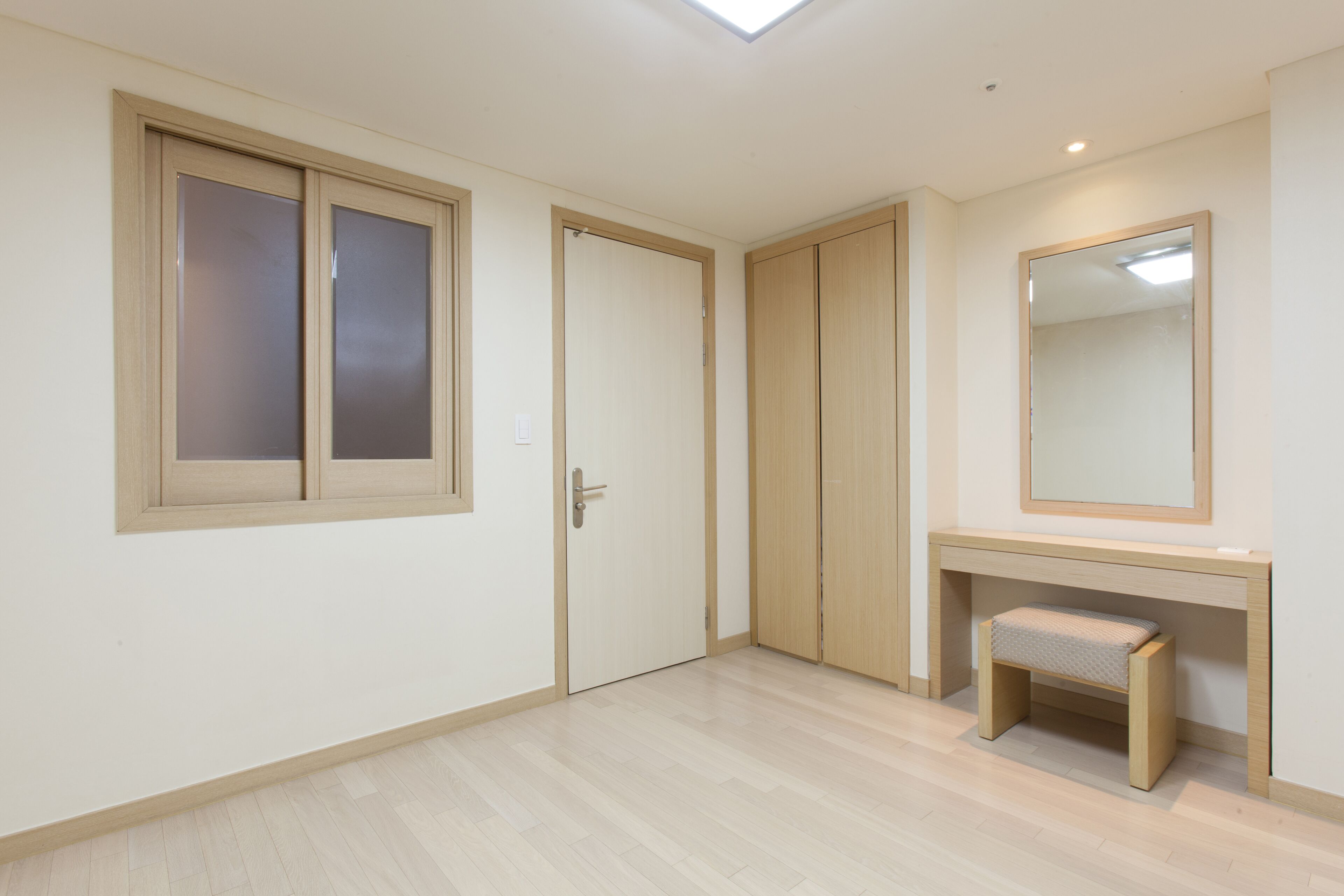 Una habitación con piso de madera, una puerta con paneles de vidrio esmerilado, un banco y un espejo en la pared.