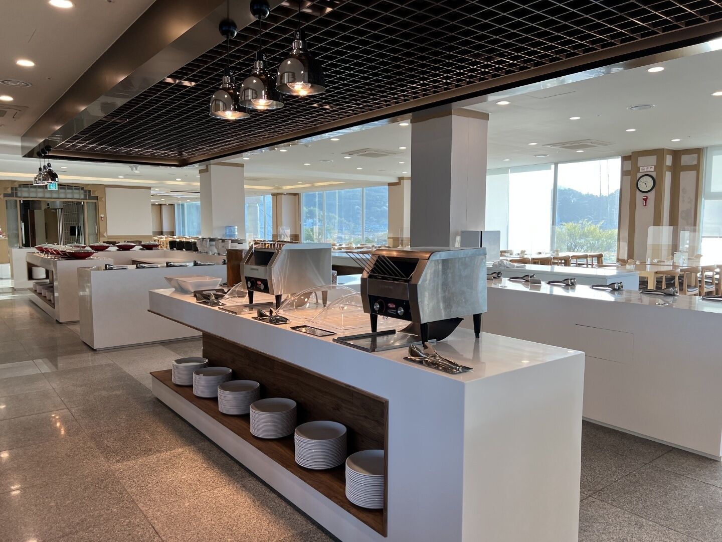 Un espace moderne dédié au petit-déjeuner, doté d’un buffet, de machines à café et offrant une vue sur l’extérieur.
