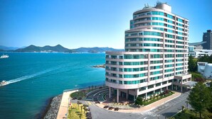 A multi-story hotel with a curved facade, located near a waterfront with a view of the sea and distant mountains. - Kumho Tongyeong Marina Resort (Tongyeong)