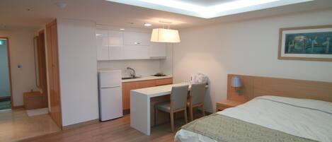 A compact hotel room with a bed, a desk, and a kitchenette.