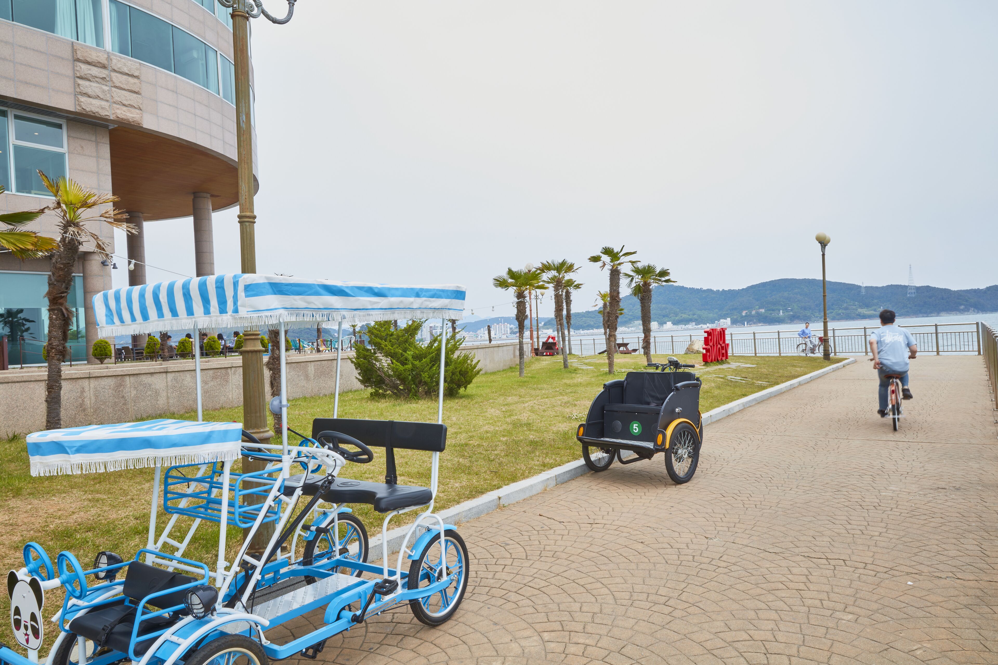 A paved walkway with a blue and white striped canopy, a black golf cart, and a person riding a bicycle.