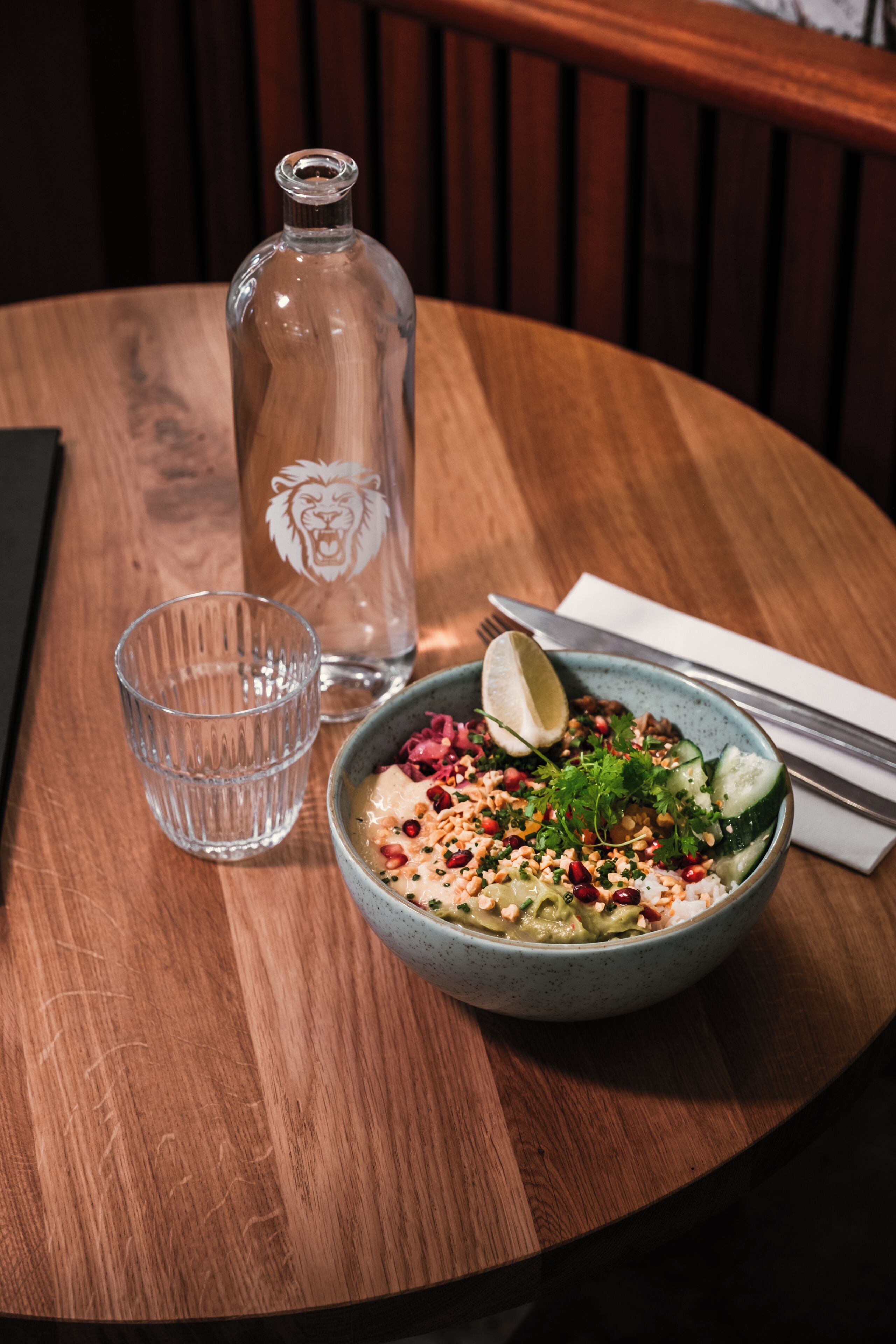 A wooden table with a bowl of food, a glass, and a bottle.