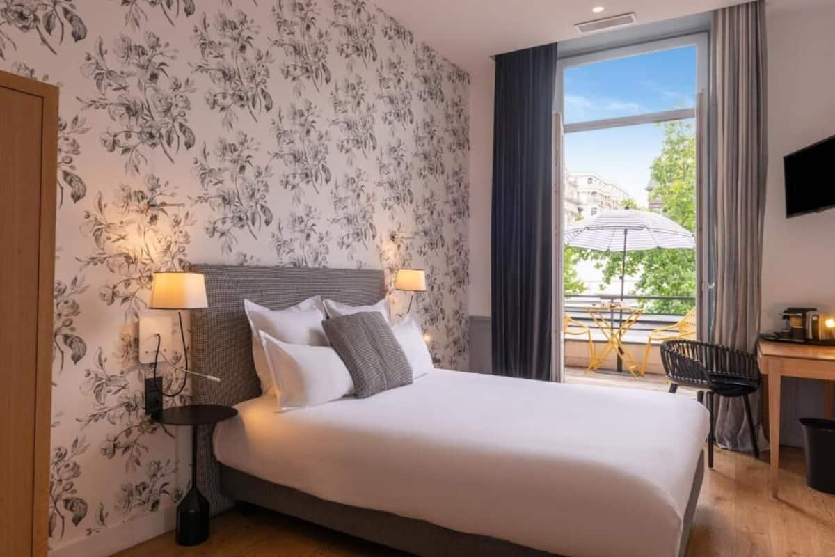 A hotel room with a large bed, two bedside lamps, a desk with a chair, and a view of the outdoors.