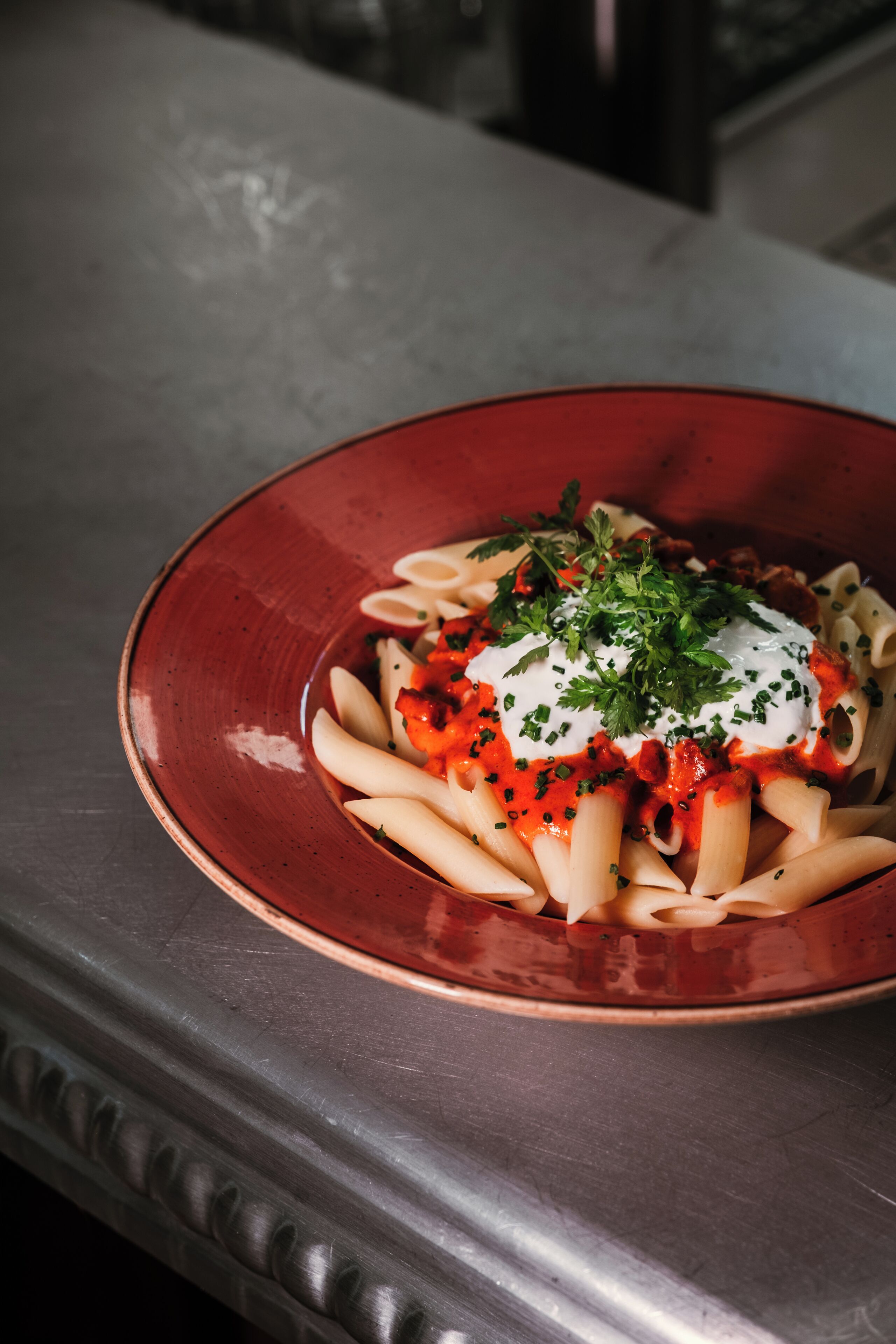 A red plate with pasta and a creamy topping on a table.