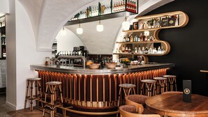 Uma área de bar com balcão curvo, banquetas e prateleiras cheias de garrafas de bebidas.