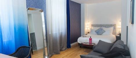A hotel room with a bed, bedside table, lamp, and a sofa.