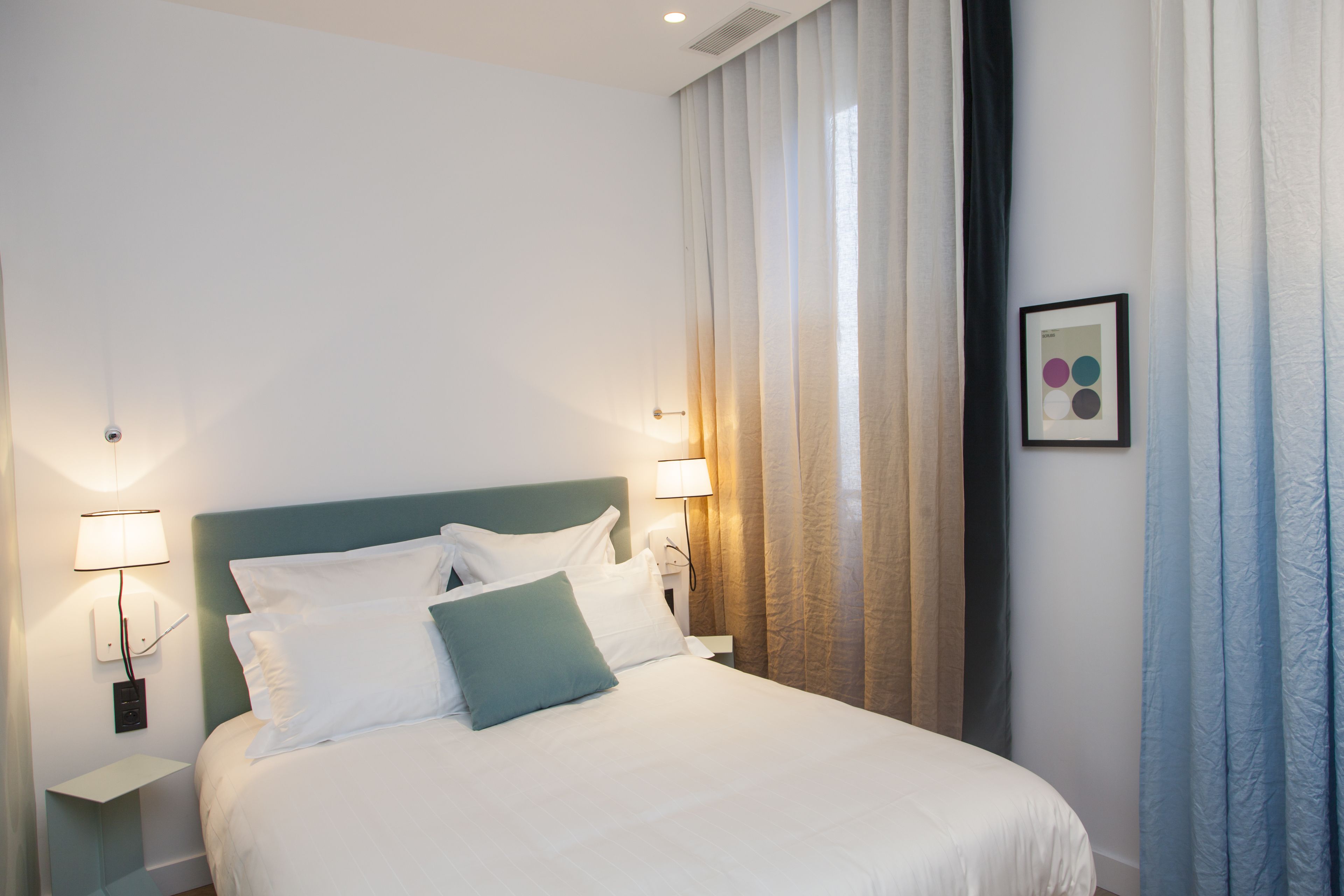 A neatly made bed with white and teal bedding, two bedside lamps, and a framed picture on the wall.
