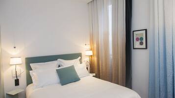A neatly made bed with white and teal bedding, two bedside lamps, and a framed picture on the wall.