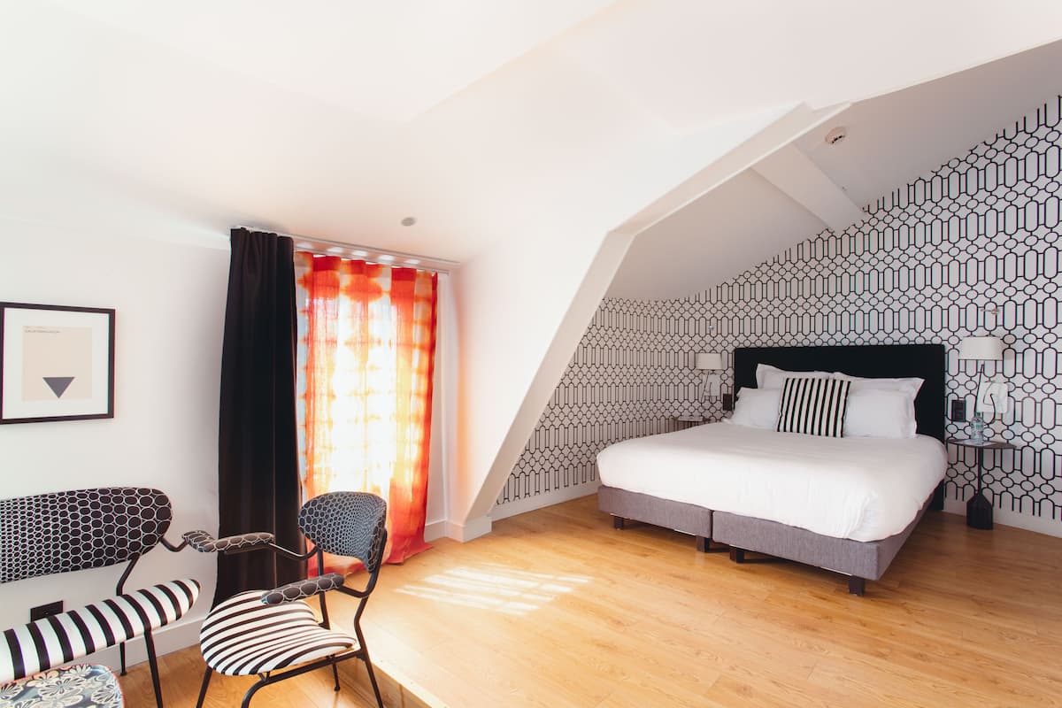 A modern bedroom with a bed, a chair, a small table, and a patterned wall.