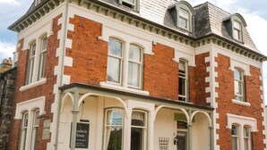 A two-story building with a white facade and red brick accents, featuring a prominent entrance with a porch and a sign reading "Goodwin House." - Goodwin House (Keswick)