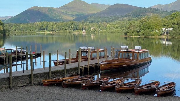 A lakeside dock with several wooden boats and a larger boat moored at the pier. - Goodwin House (Keswick)